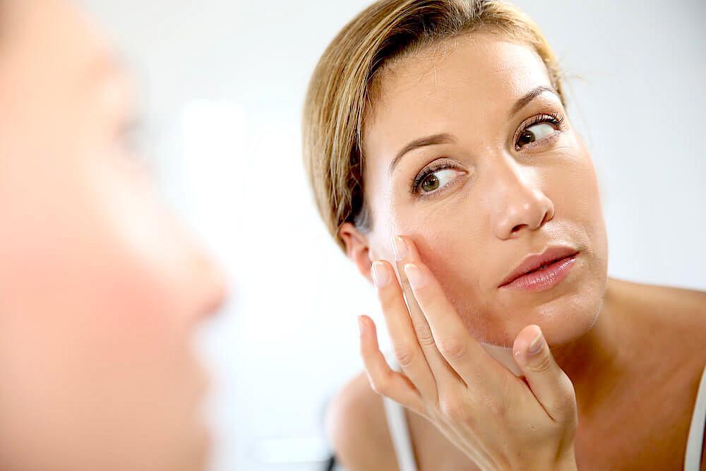 Woman examining skin in mirror