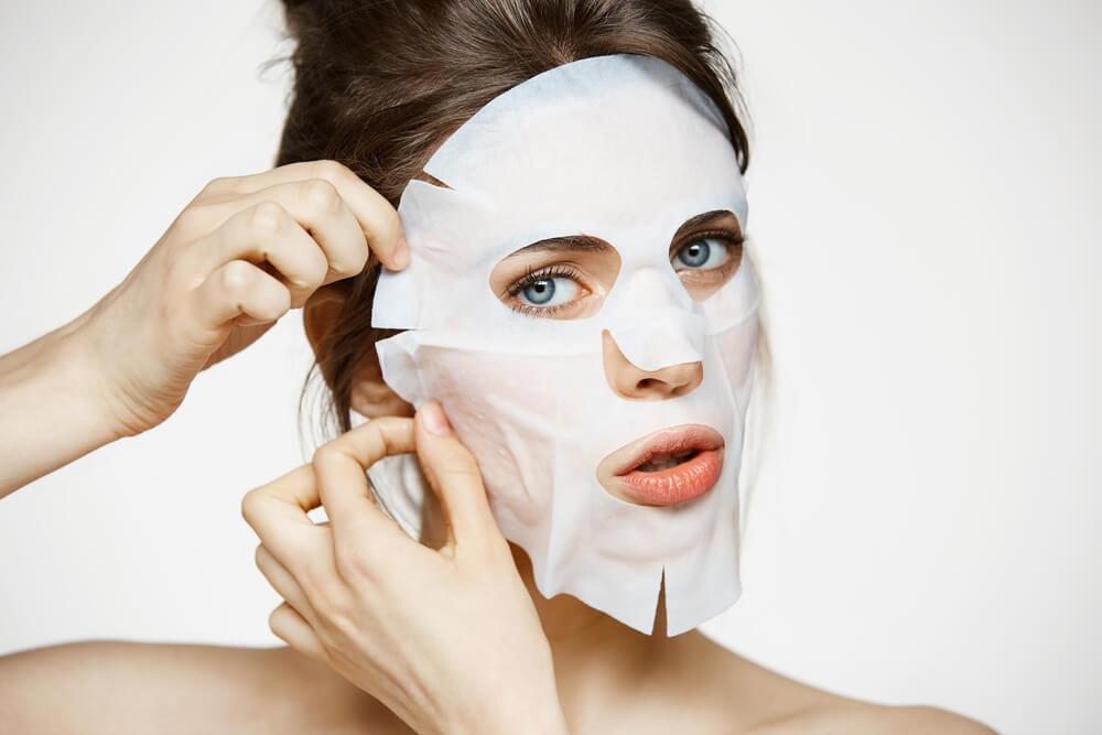 Young woman applying sheet mask to face