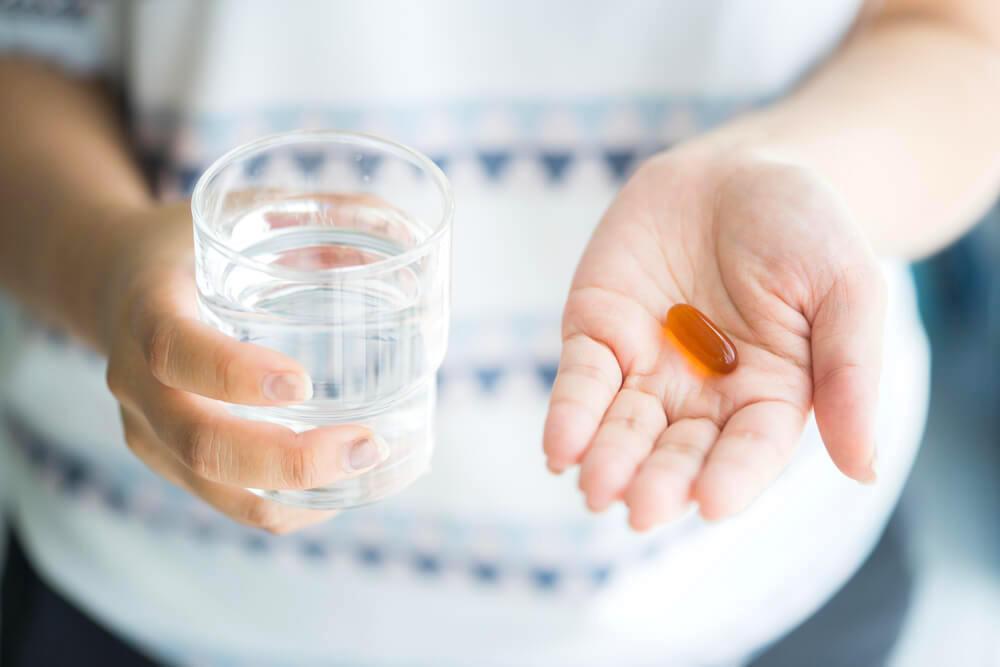 A glass of water and a small Omega-3 pill in unknown woman's hand