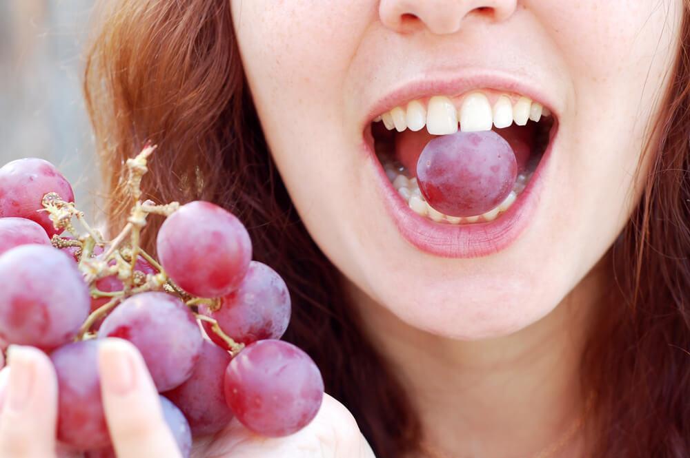 Woman with red grape in mouth