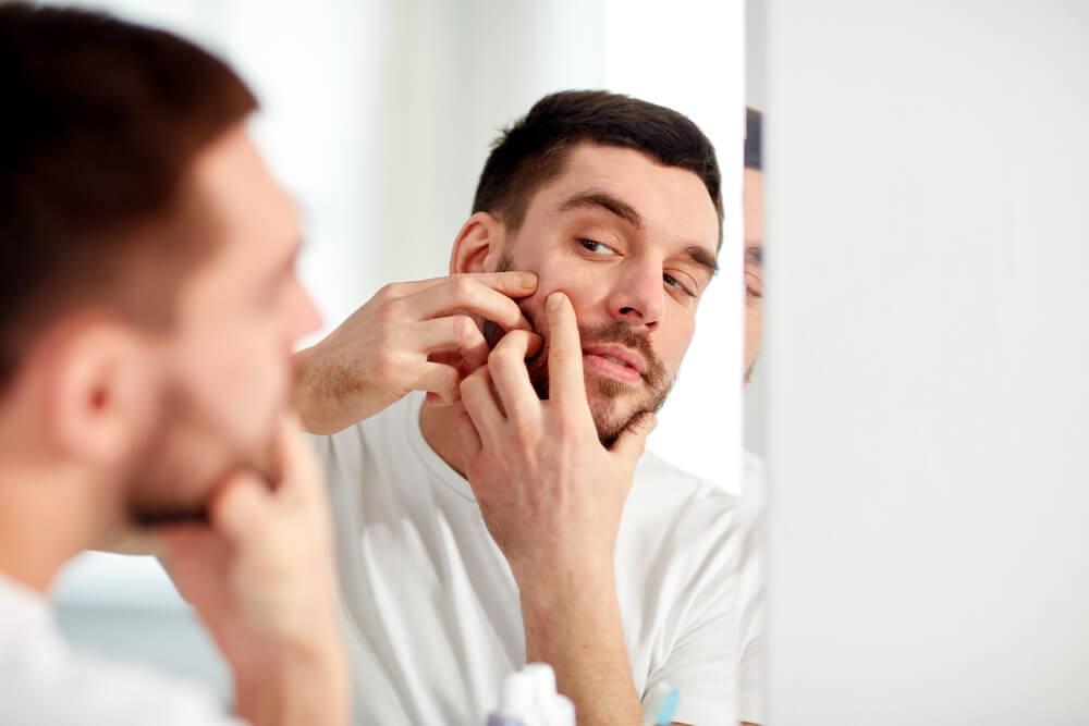 Man looking at pimple in mirror